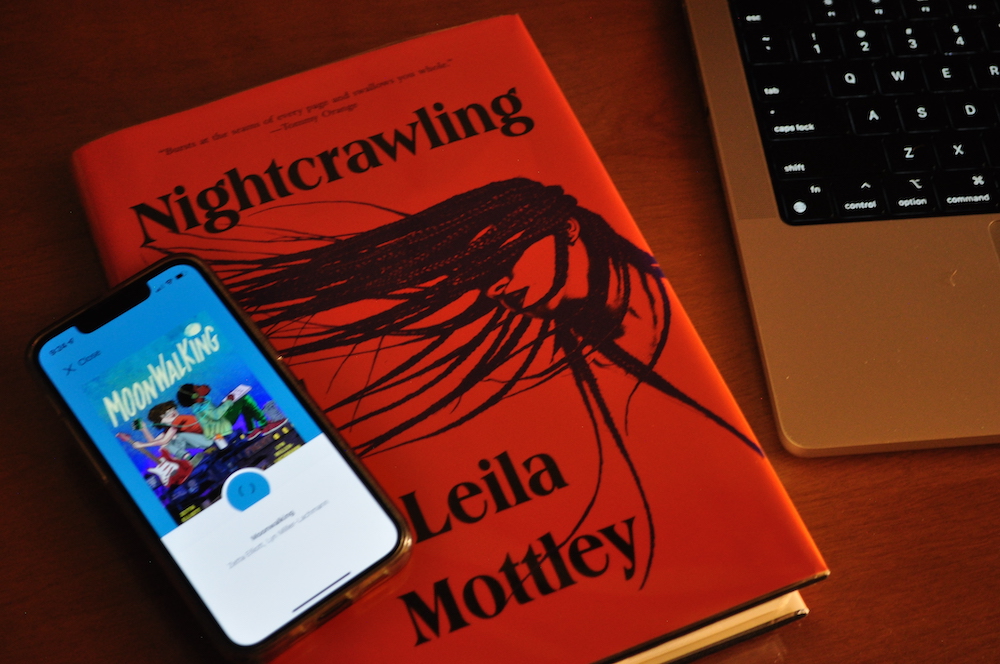 Image of Nightcrawling physical book and Moonwalking digital cover on my phone on my desk in the dim lamp light tonight