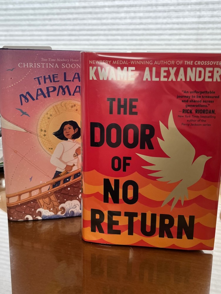 Two books standing on a desk - The Door of No Return by Kwame Alexander and The Last Mapmaker by Christina Soontornvat